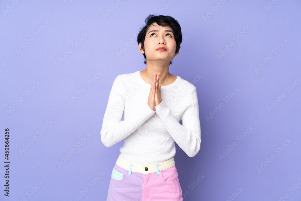 Young Vietnamese woman with short hair over isolated purple background keeps palm together. Person asks for something Young Vietnamese woman with short hair over isolated purple background keeps palm together. Person asks for something