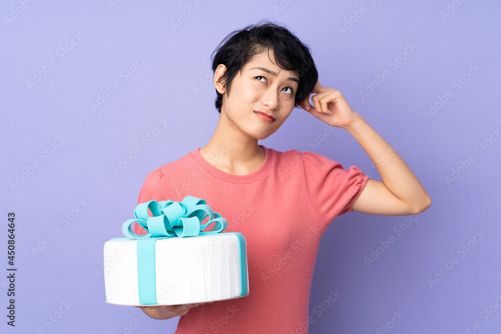 Young Vietnamese woman with short hair holding a big cake over isolated purple background having doubts and with confuse face expression Young Vietnamese woman with short hair holding a big cake over isolated purple background having doubts and with confuse face expression