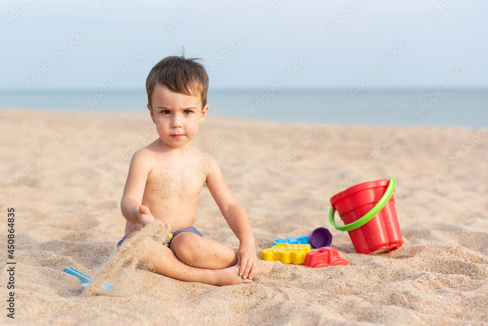 Adorable kid plays on the seashore in the sand with toys. Summer holidays Adorable kid plays on the seashore in the sand with toys. Summer holidays