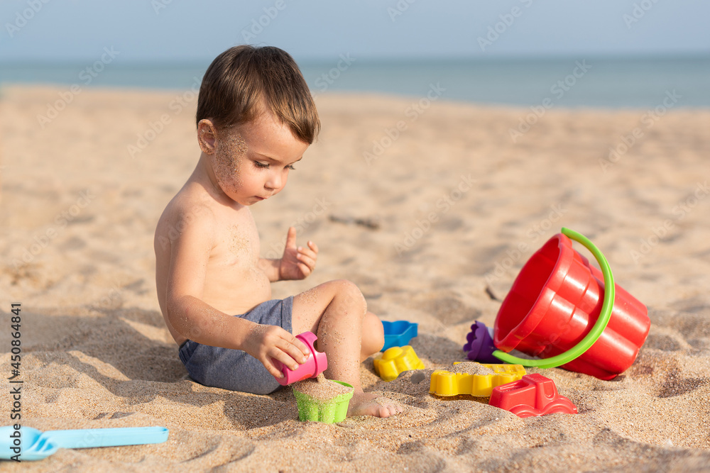 Adorable kid plays on the seashore in the sand with toys. Summer holidays Adorable kid plays on the seashore in the sand with toys. Summer holidays