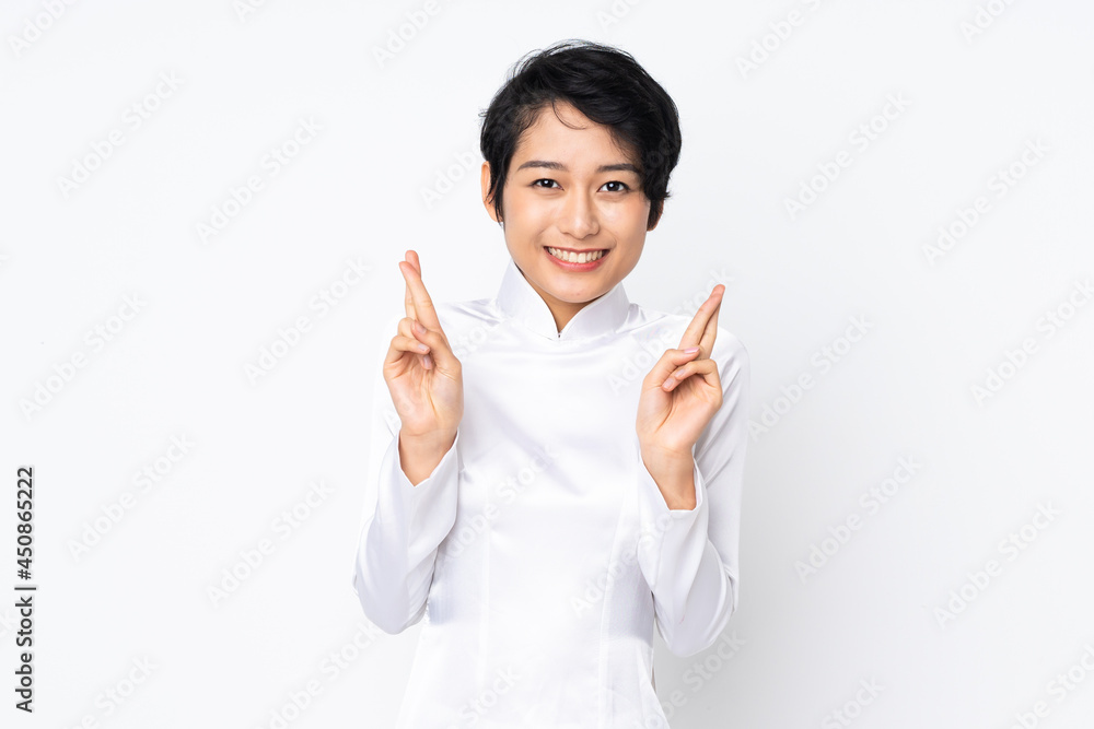 Young Vietnamese woman with short hair wearing a traditional dress over isolated white background with fingers crossing and wishing the best Young Vietnamese woman with short hair wearing a traditional dress over isolated white background with fingers crossing and wishing the best