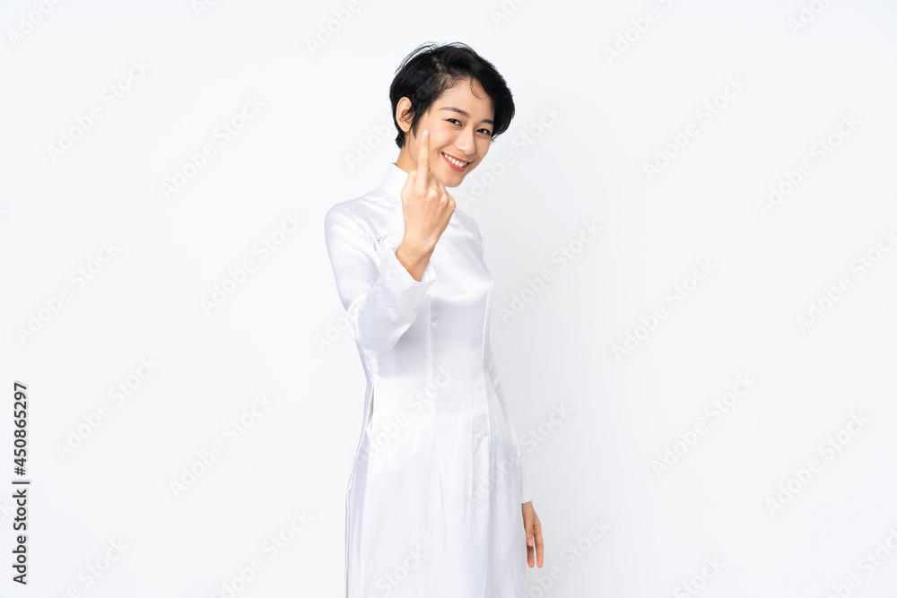 Young Vietnamese woman with short hair wearing a traditional dress over isolated white background doing coming gesture Young Vietnamese woman with short hair wearing a traditional dress over isolated white background doing coming gesture