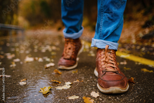 feet of a woman walking along asphalt road in autumn forest in the rain. Pair of shoe on slippery road in the fall. Abstract empty blank of the autumn weather