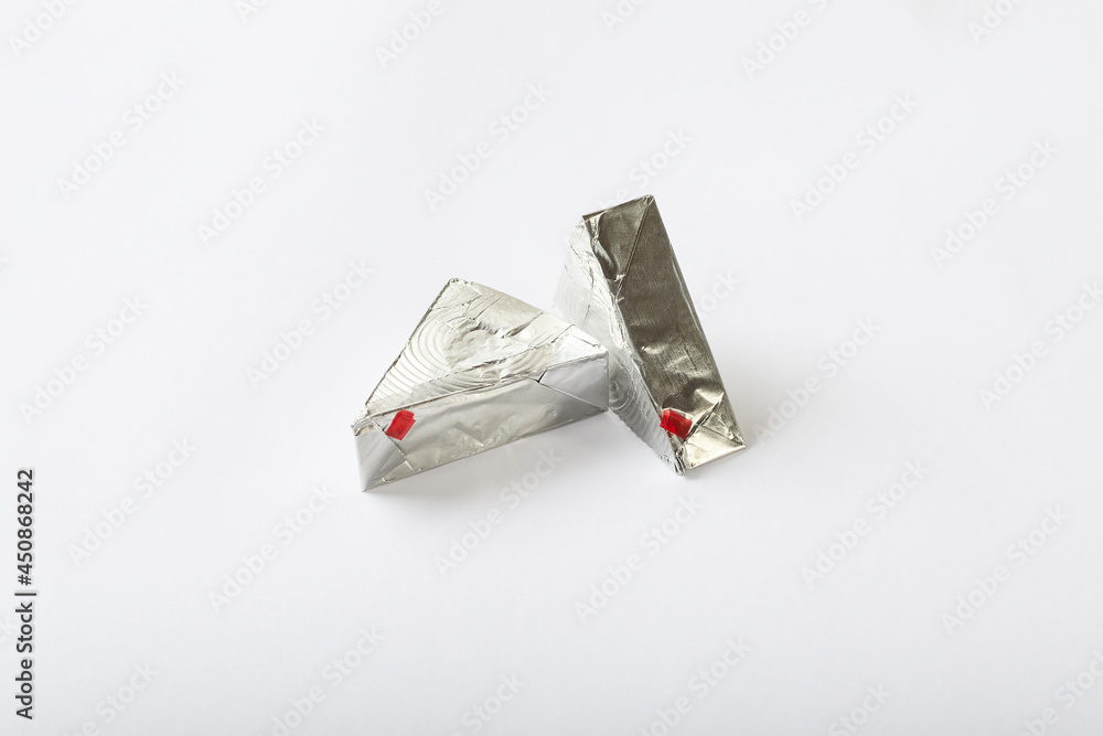 Triangular cream cheeses wrapped in aluminum foil on a white background. Portioned triangular