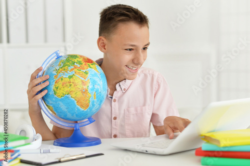Cute boy using laptop while holding globe