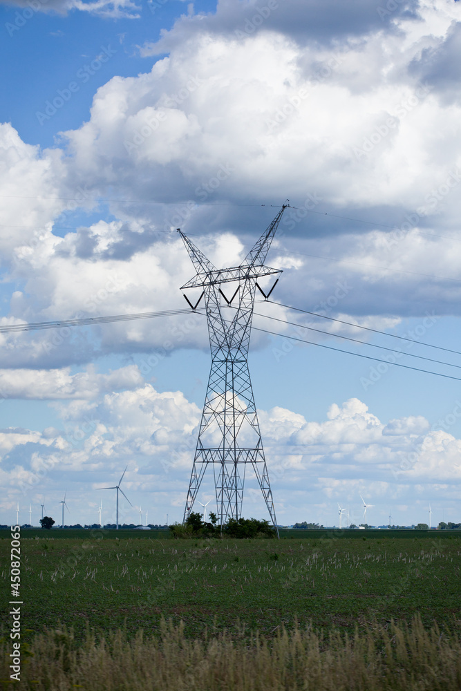 High tension tower stands out against beautiful cloudy blue skies in rural USA with wind farm in the distant horizon. High tension tower stands out against beautiful cloudy blue skies in rural USA with wind farm in the distant horizon.