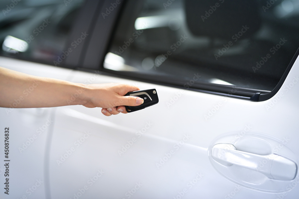 Women's hand presses on remote control unlocks car door alarm systems. Vehicle convenience safety security system.  New technology car keys remote concept.