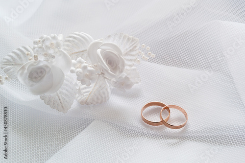 Gold wedding rings and white artificial flowers to decorate the hairstyle on white cloth under a white mesh veil.