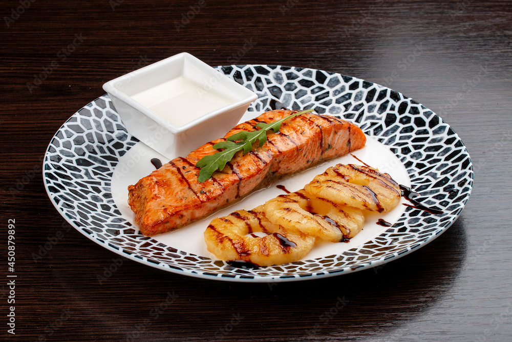 Salmon with cream sauce and grilled pineapple. On a wooden background