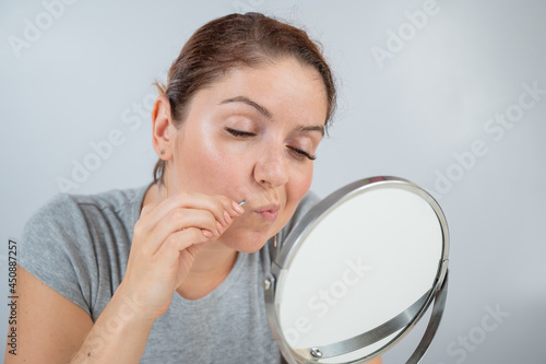 Valokuva Caucasian woman looks in the mirror and removes the mustache herself with the help of tweezers