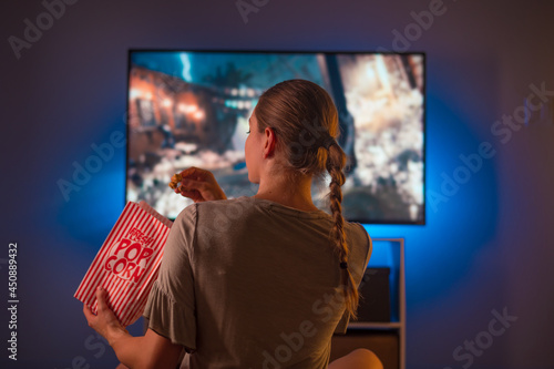 Foto A young blonde girl is watching TV and eating popcorn