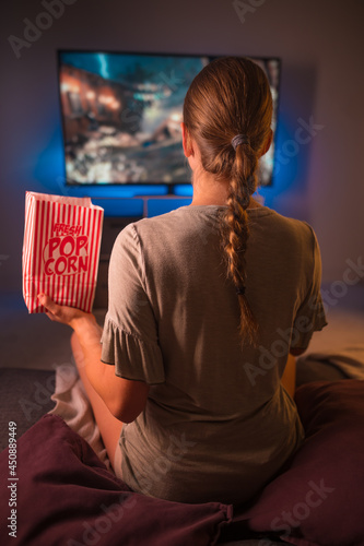 The girl is watching TV with popcorn in her hand. Close-up. Shooting from the back. Color image. Film industry, advertising, banner, poster.