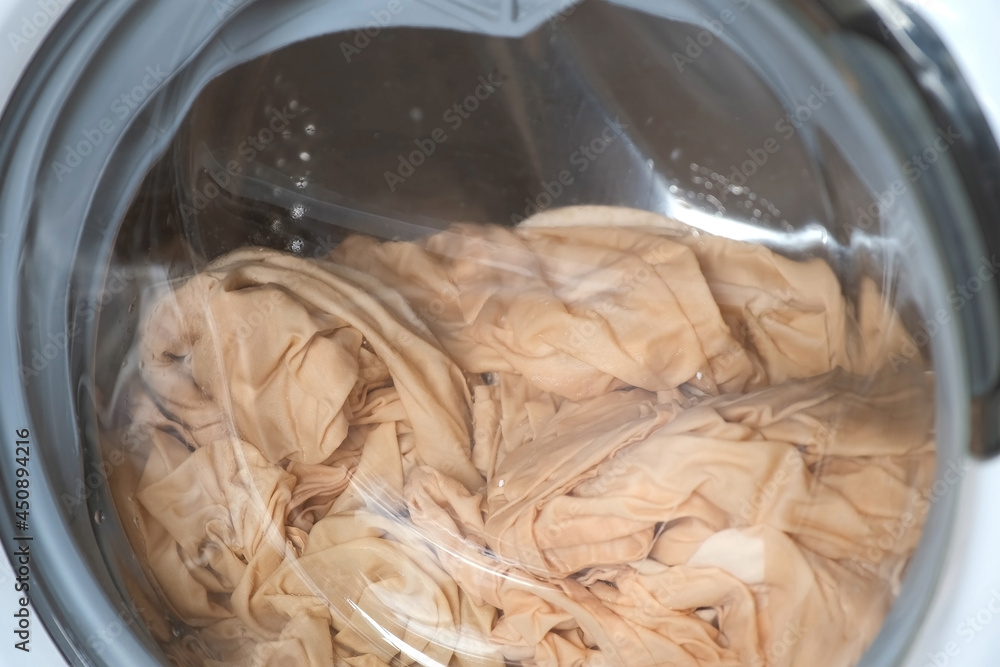 Washing machine with beige bed linen inside is working, laundry at home ...