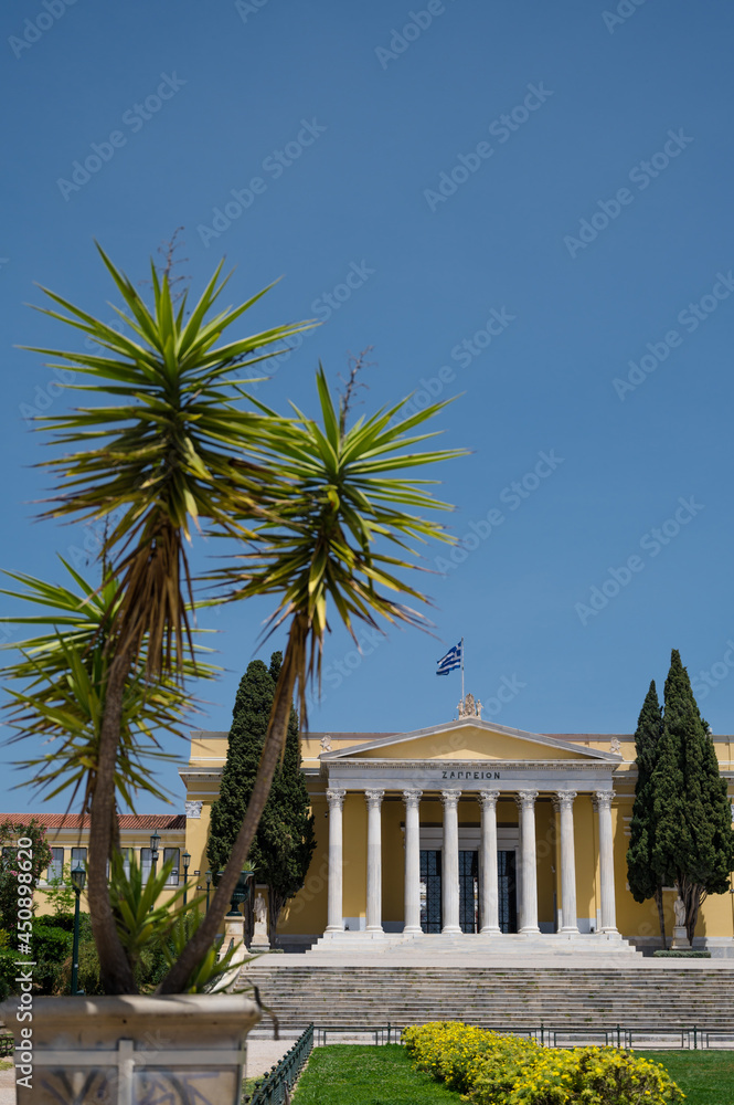 Front view of the Zappeion Hall in the National Gardens of Athens. Blue sky. Green trees. Classical architecture.