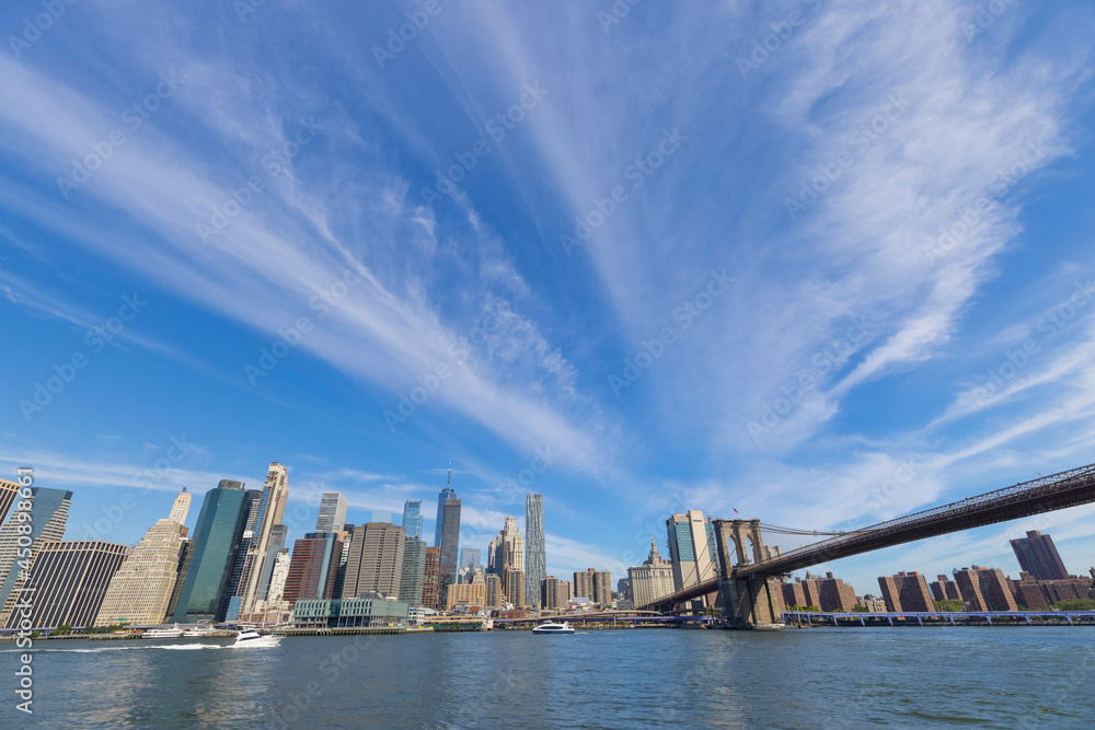 Unique shape summer clouds float over the Lower Manhattan skyscraper and Brooklyn Bridge along the East River on June 20, 2021 in the Brooklyn Borough of New York City NY USA.