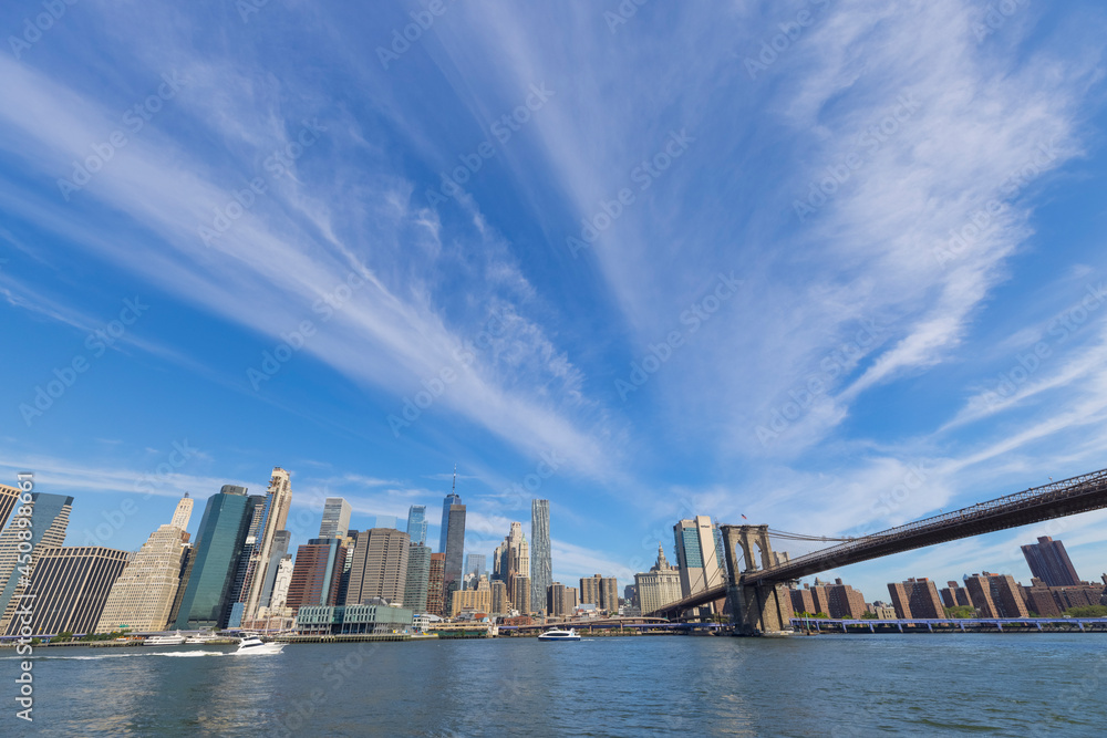Fototapeta premium Unique shape summer clouds float over the Lower Manhattan skyscraper and Brooklyn Bridge along the East River on June 20, 2021 in the Brooklyn Borough of New York City NY USA.
