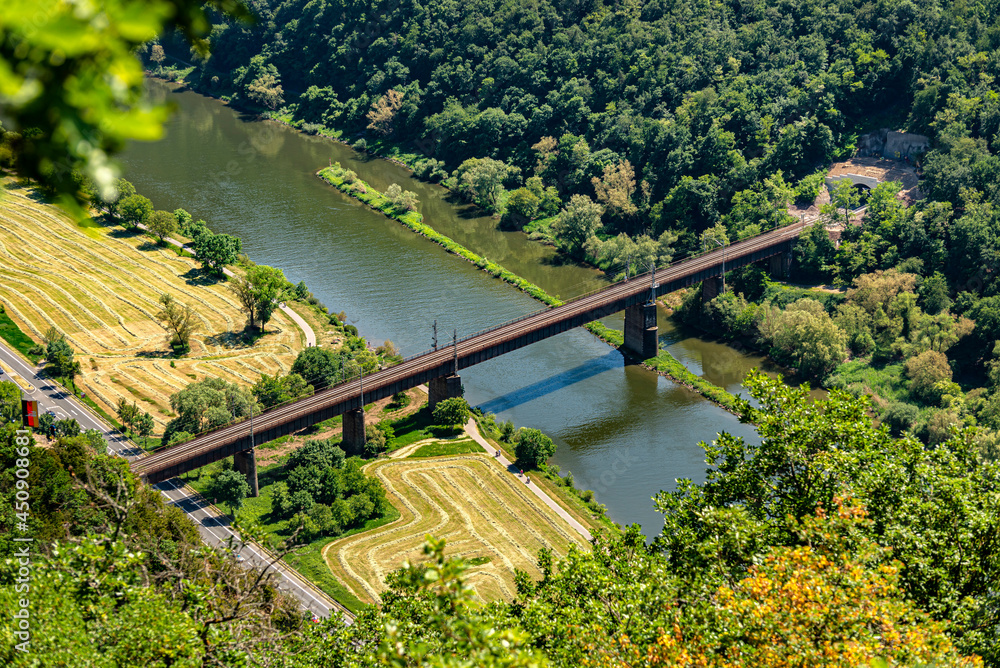 The steel truss structure of the railway bridge seen from above, in the background there are hills overgrown with forest.