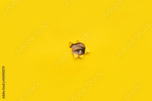 Fotografía Eye looking through a hole in a yellow paper