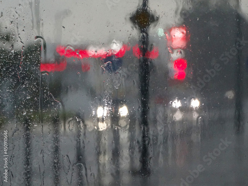 Wet glass surface after rain, soft focus. Night city, street and cars lighting blurry. Water drops. Nostalgic. Petrol station and signboard defocused by rain drops on a window glass.