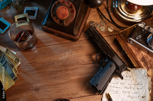 Private detective's desk, noir still life with a vintage phone, typewriter, lamp, gun and retro photos