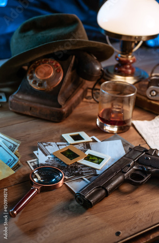 Private detective's desk, noir still life with a vintage phone, typewriter, lamp, gun and retro photos