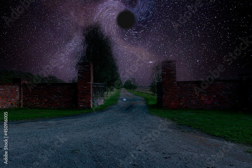 Brama za którą jest długo polna droga. Jest noc, niebo jest rozgwieżdżone, w centralnym miejscu jest wizualizacja czarnej dziury.