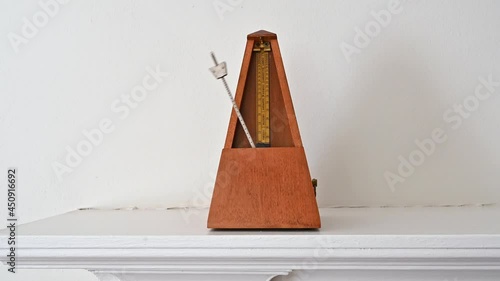 An old fashioned metronome beating at a Largo pace on a white shelf.