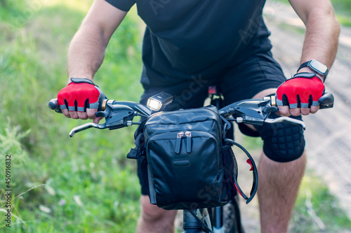 Cyclist in gloves on a mountain bike with a bag on the handlebars.
