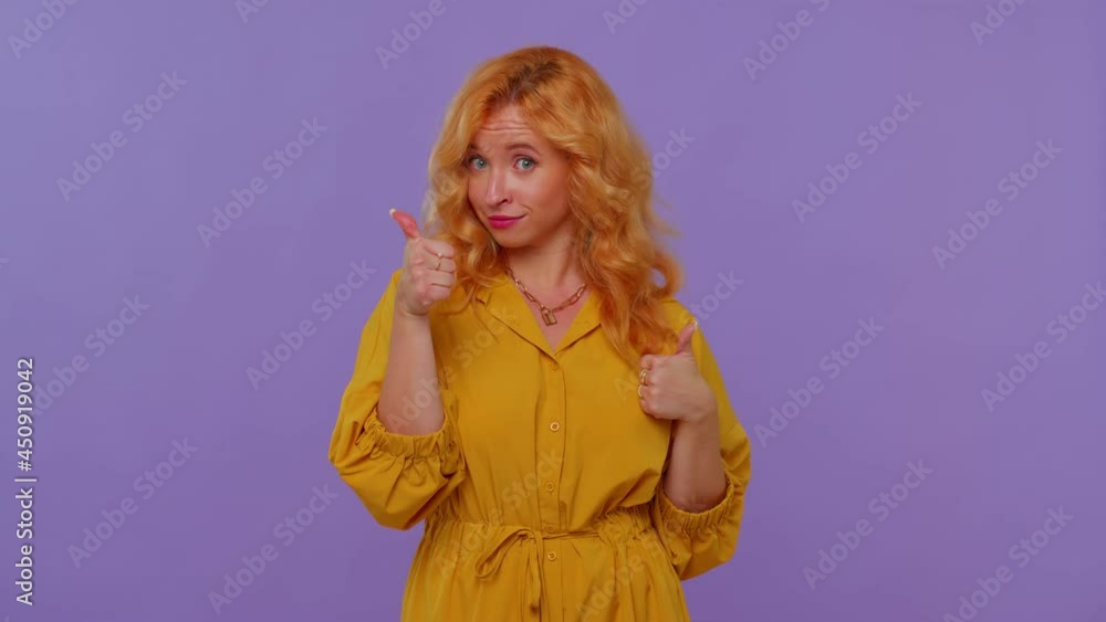 Long haired lovely girl in yellow dress raises thumbs up agrees with something or gives positive reply recommends advertisement likes good. Young fashionable woman isolated on purple studio background Long haired lovely girl in yellow dress raises thumbs up agrees with something or gives positive reply recommends advertisement likes good. Young fashionable woman isolated on purple studio background