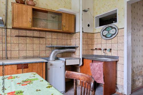 Example of Old Soviet Russian poor kitchen interior in Khruschev House. Aged  sideboard, table, chairs. Shabby floor. Tattered tiles on the wall. Apartment of pensioners.