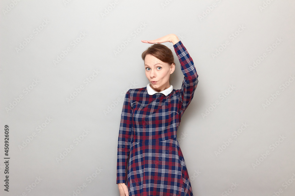Surprised girl is holding hand above head and measuring her height Surprised girl is holding hand above head and measuring her height