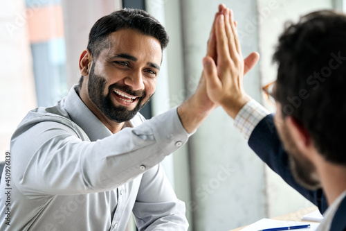 Fotografie Indian happy smiling multiracial professional ceo businessman giving highfive to business partner after financial acquisition bank bargain contract at office