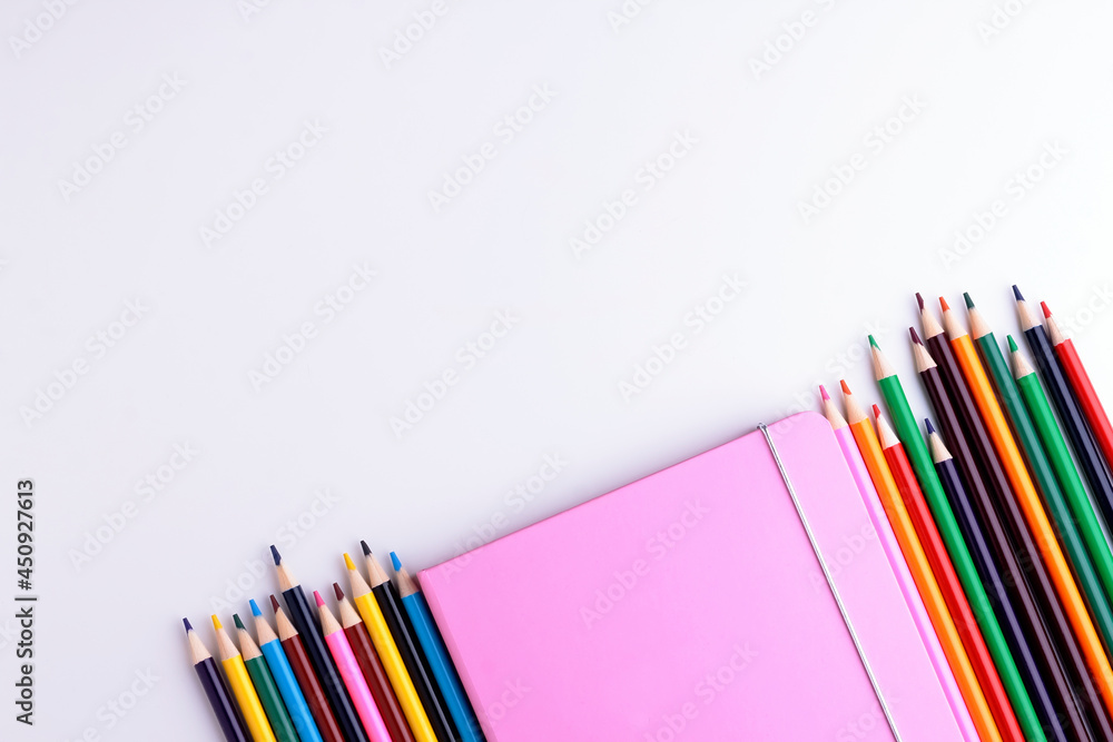 Fototapeta premium Pink notebook and color pencils on white background. Scool equipment on white. Copy space.