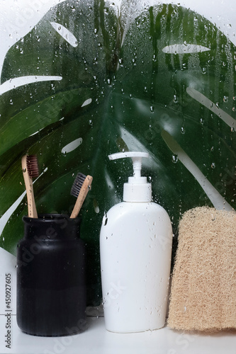 Wallpaper Mural Soap bottle, teeth brushes, shower sponge behind  wet glass. White liquid soap bottle with shower accessories in the shower with palm Monstera leaf. Torontodigital.ca