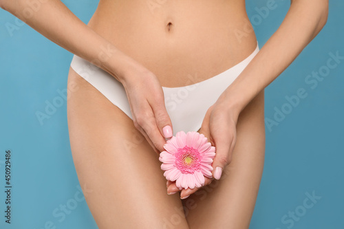 Woman in white panties with gerbera flower on light blue background, closeup photo