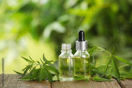 Hemp leaves, bottles of CBD oil and THC tincture on wooden table