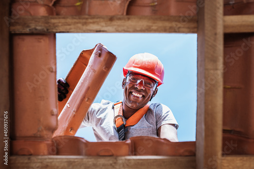 Canvastavla Latin worker installing yellow ceramic roofing tiles mounted on wooden boards covering residential building roof under construction