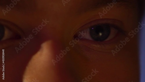 Extreme close up of human eyes under neon light. Macro eyes of young man watching movie tv film, video at night. Reflection on his face