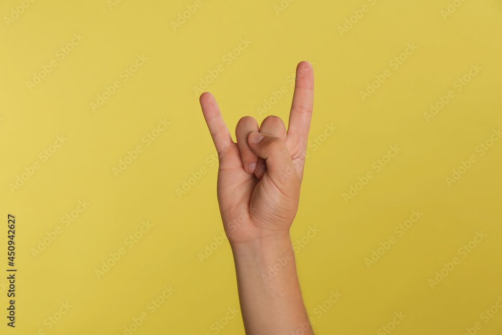 Naklejka premium Teenage boy showing rock gesture on yellow background, closeup