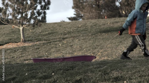 Boy pulls a sled in a snowless winter hoping for snow to come.