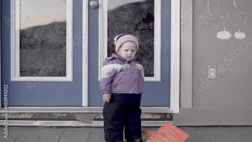Small child waits outside with a snow shovel in a snowless winter