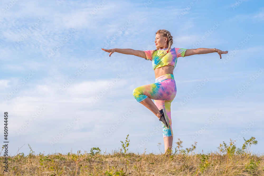 Young beautiful girl is engaged in gymnastics on a green meadow against the background of a blue summer sky. Outdoor sports. Positive emotions. Young beautiful girl is engaged in gymnastics on a green meadow against the background of a blue summer sky. Outdoor sports. Positive emotions.