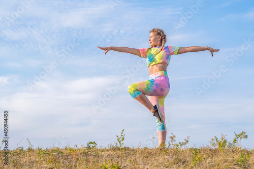 Young beautiful girl is engaged in gymnastics on a green meadow against the background of a blue summer sky. Outdoor sports. Positive emotions.
