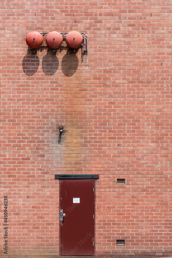 Red door, red brick wall and three fire alarm bells