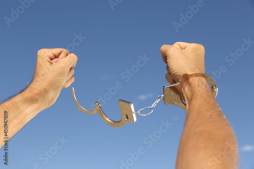 Man in handcuffs against blue sky outdoors, closeup
