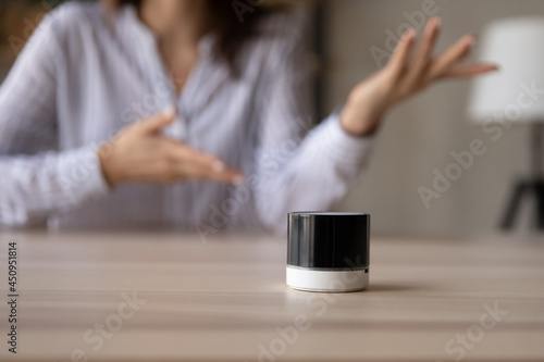 Crop close up of small portable modern speaker on table at home, woman talk activated digital voice assistant. Female client or customer use wireless electronic audio device listen to music.