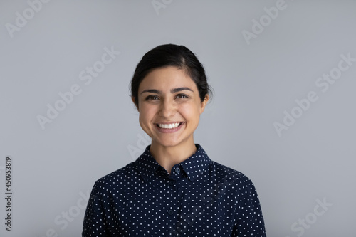 Headshot portrait of smiling millennial Indian woman isolated on grey studio background feel optimistic. Profile picture of happy young biracial female client customer show white healthy teeth.