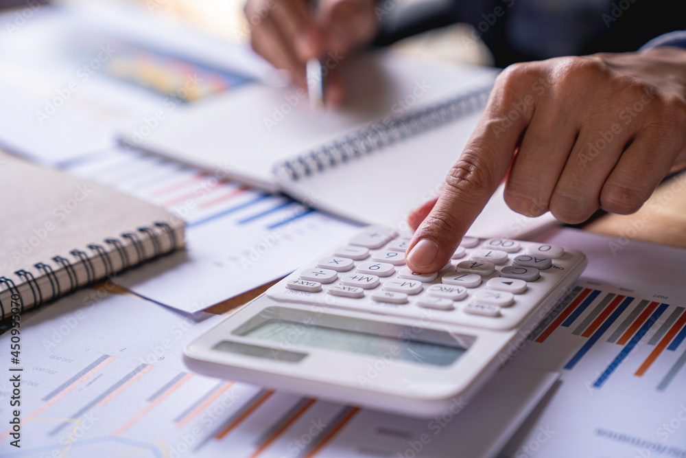 Accountant or banker working process, a Businesswoman using a calculator to calculate the numbers of statistic business profits growth rate on documents graph data, his desk in an office. Accountant or banker working process, a Businesswoman using a calculator to calculate the numbers of statistic business profits growth rate on documents graph data, his desk in an office.