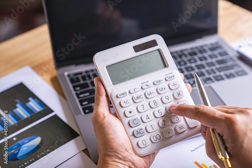 Accountant or banker working process, a Businesswoman using a calculator to calculate the numbers of statistic business profits growth rate on documents graph data, his desk in an office.