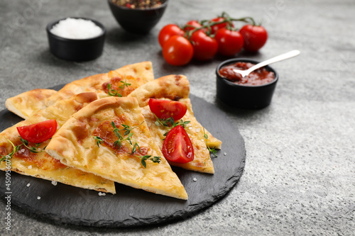 Cut delicious khachapuri with cheese, thyme, tomatoes and sauce on grey table photo